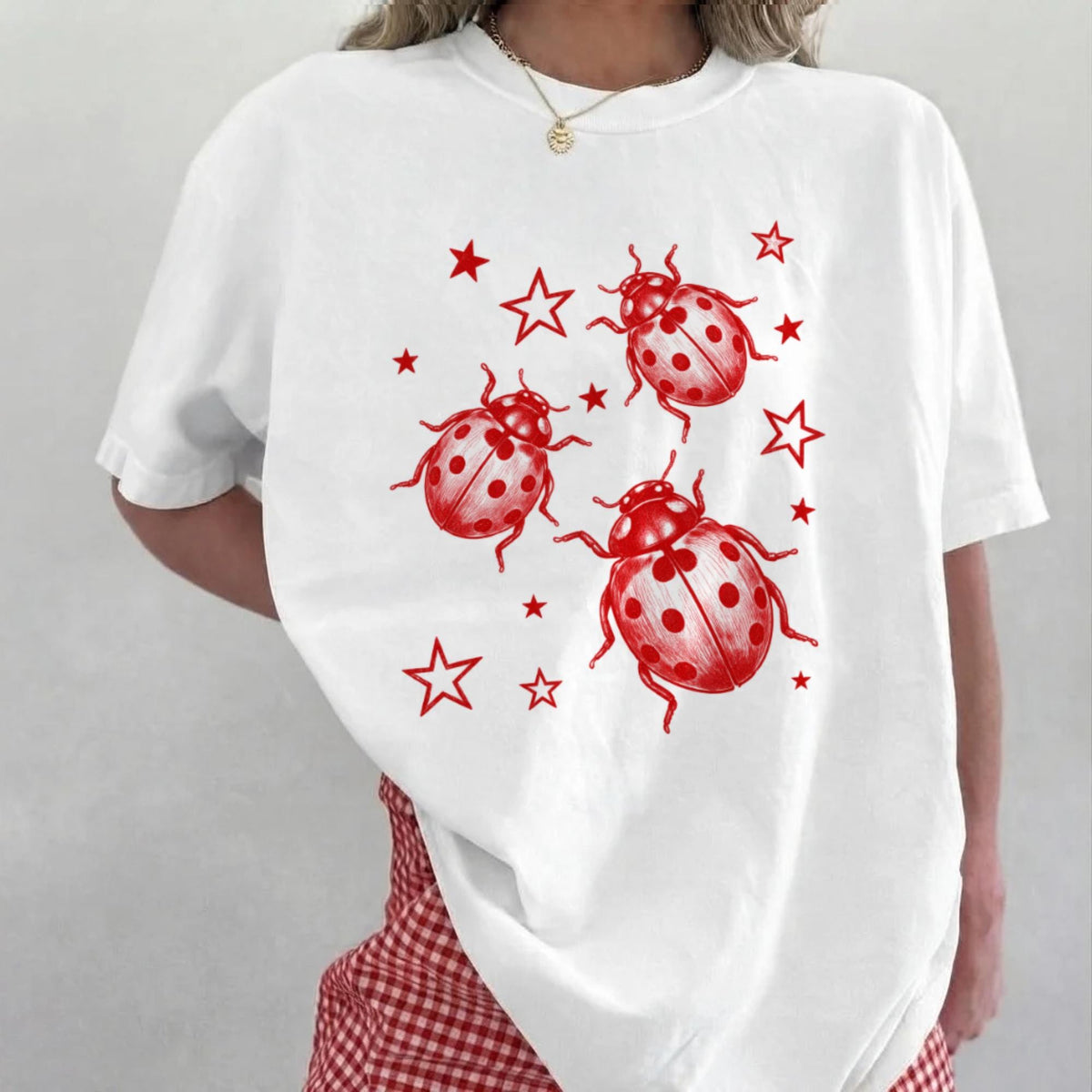 White T-shirt with three red ladybugs and scattered red stars.