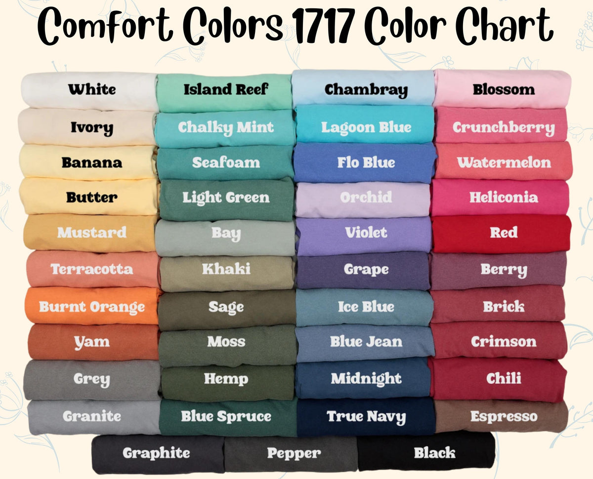 May include: A Comfort Colors 1717 color chart displaying folded fabric swatches in various shades. The text reads Comfort Colors 1717 Color Chart, followed by labels for colors including White, Ivory, Banana, Butter, Mustard, Terracotta, Burnt Orange, Yam, Grey, Granite, Graphite, Island Reef, Chalky Mint, Seafoam, Light Green, Bay, Khaki, Sage, Moss, Hemp, Blue Spruce, Pepper, Chambray, Lagoon Blue, Flo Blue, Orchid, Violet, Grape, Ice Blue, Blue Jean, Midnight, True Navy, Blossom, Crunchberry, Watermelon