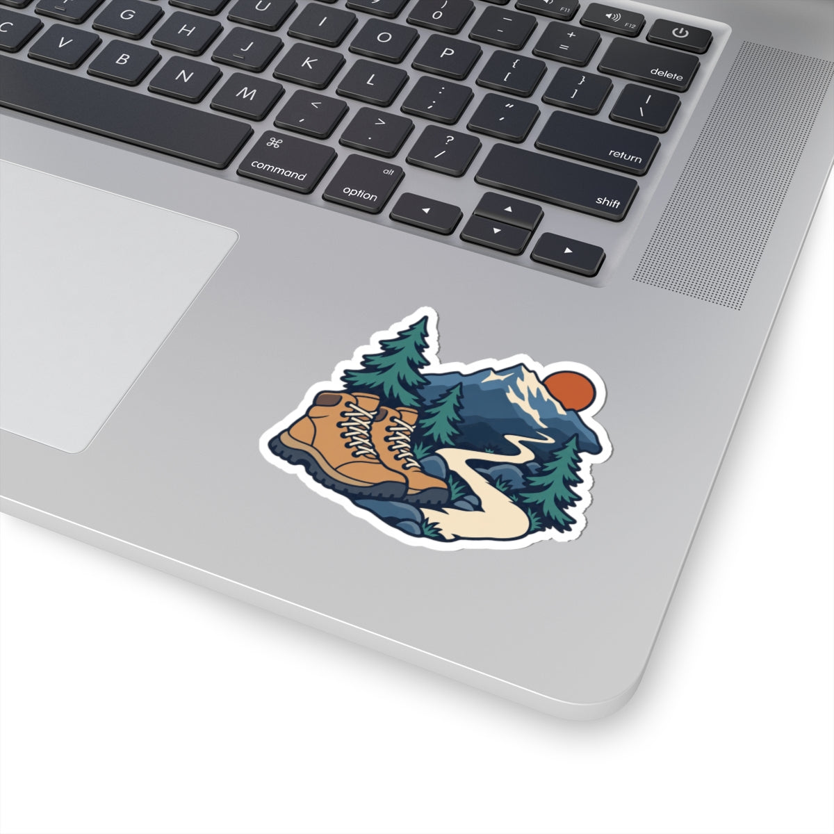 Hiking boots, mountain trail and fir trees sticker shown on a silver laptop beside the keyboard