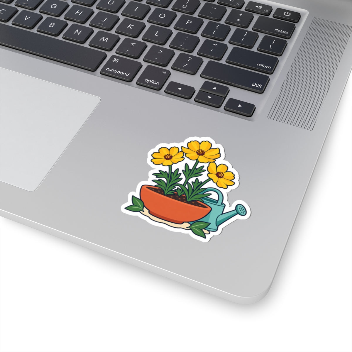 Yellow flower pot and teal watering can sticker shown on a silver laptop beside the keyboard