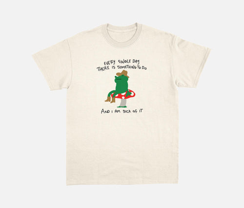 Natural T-shirt with a cowboy frog on a mushroom and a humorous daily-task quote.