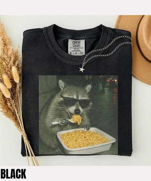 Black T-shirt with a sunglasses-wearing raccoon eating macaroni and cheese.