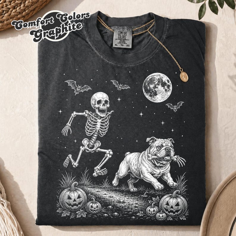 Graphite T-shirt with a skeleton chasing an English bulldog among Halloween pumpkins.