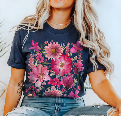 May include: Navy blue t-shirt featuring a vibrant floral design in shades of pink and magenta. The botanical illustration includes various flowers and foliage, creating a colorful and artistic composition. The shirt has rolled-up sleeves.