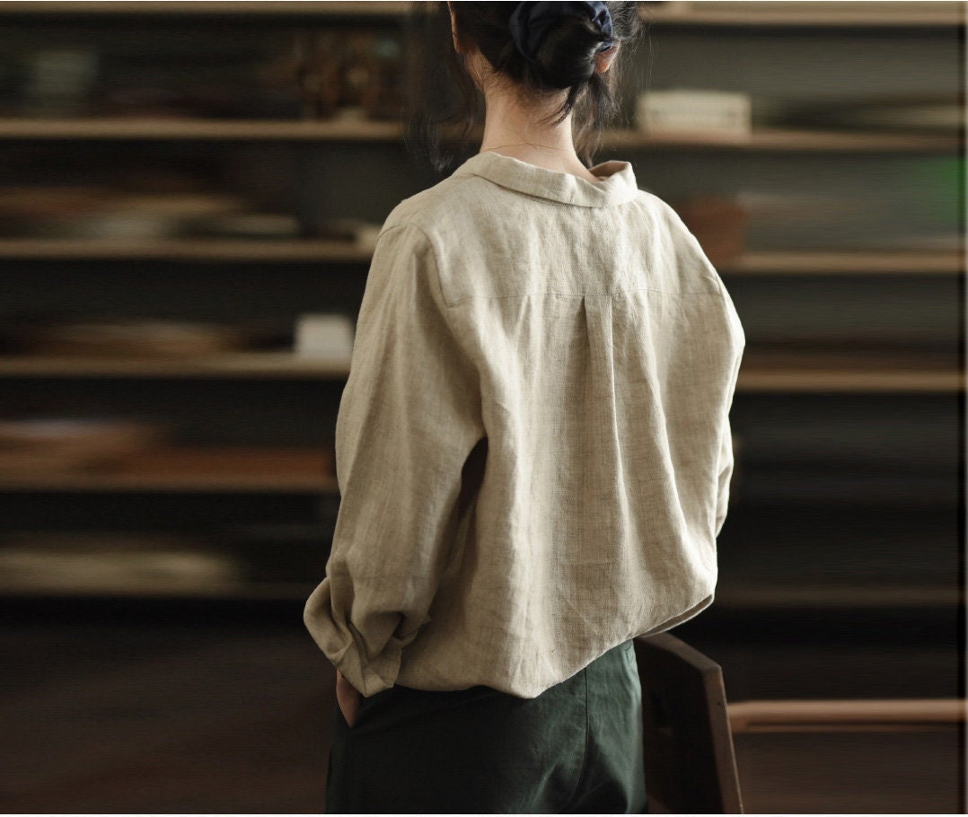 May include: A beige linen shirt with a long sleeve and a button-up collar. The shirt is loose-fitting and has a relaxed silhouette.