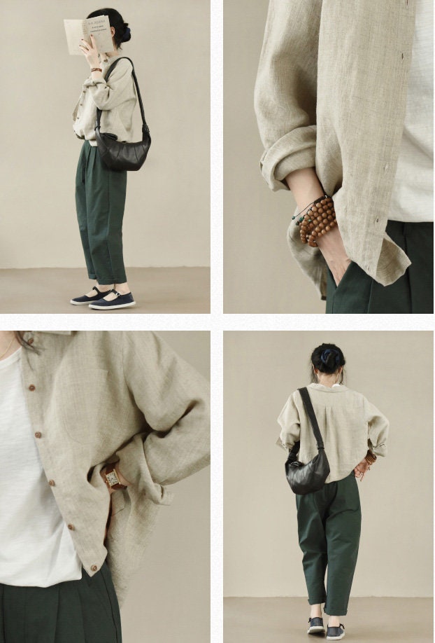 May include: A woman is wearing a light beige linen shirt with a dark green pair of pants. She is carrying a black leather shoulder bag.