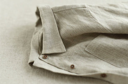May include: A close-up of a light beige linen shirt with a button-down collar and a pocket. The shirt has a subtle texture and is made of a natural fabric.