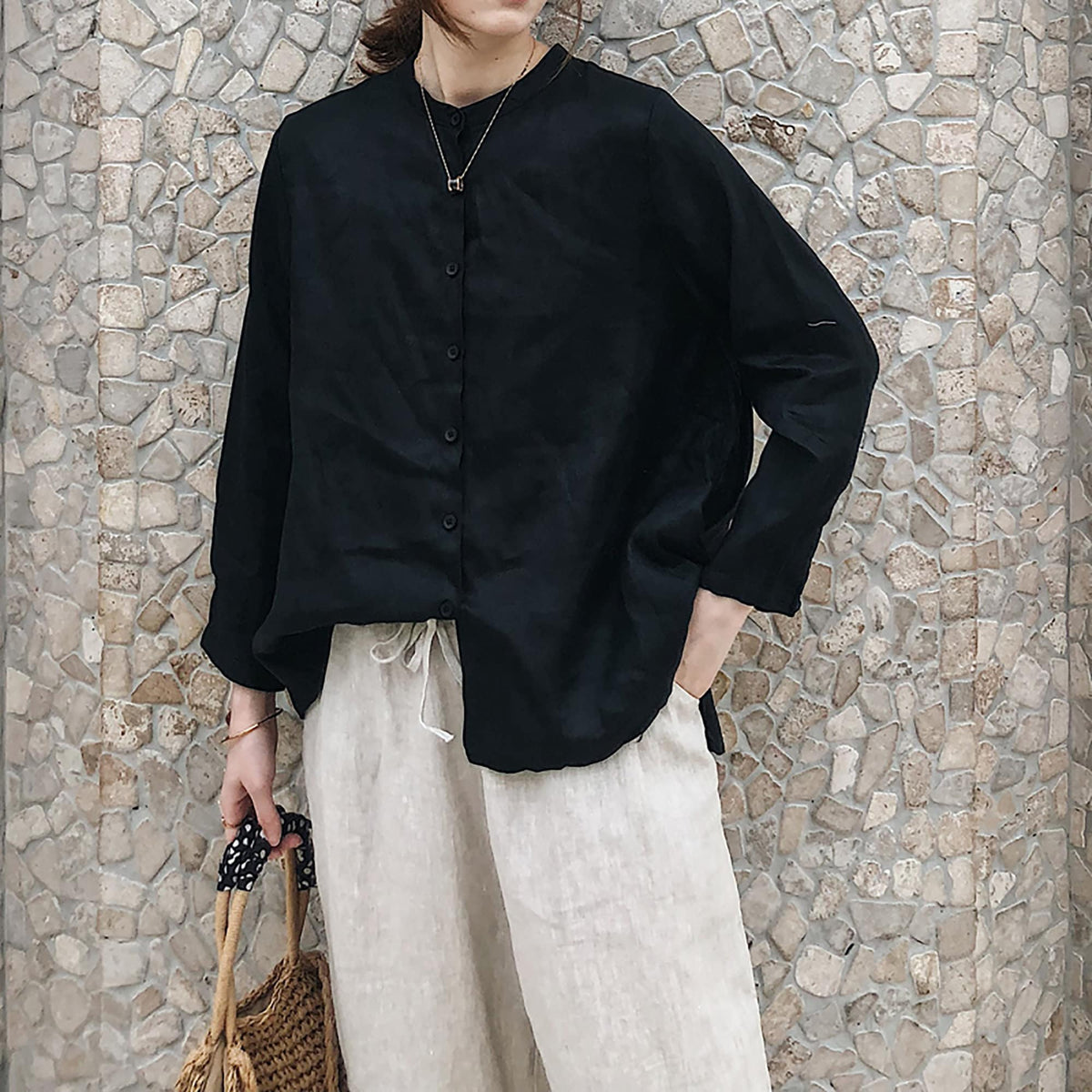 May include: A black long-sleeved button-up shirt with a mandarin collar and a relaxed fit. The shirt is paired with beige linen pants.
