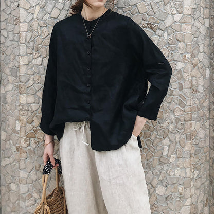 May include: A black long-sleeved button-up shirt with a mandarin collar and a relaxed fit. The shirt is paired with beige linen pants.