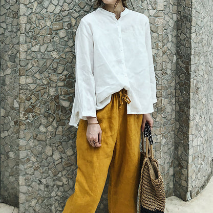 May include: A white linen shirt with a mandarin collar and long sleeves, paired with mustard yellow linen pants and a woven straw tote bag with black accents.