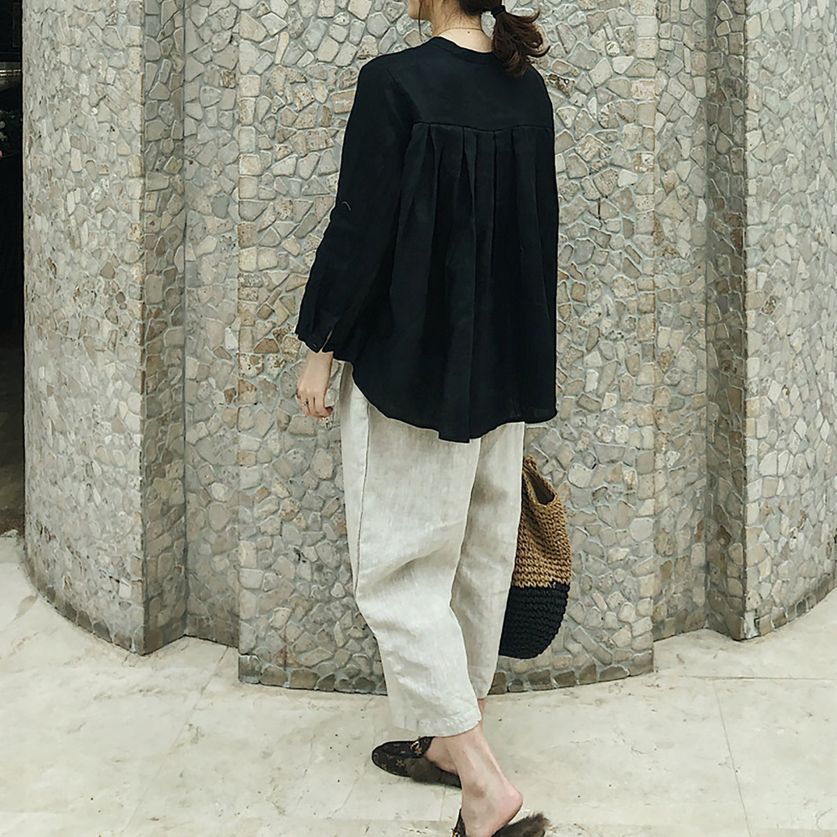 May include: A black, long-sleeved blouse with a pleated back and a relaxed fit. The blouse is paired with beige, wide-leg pants.