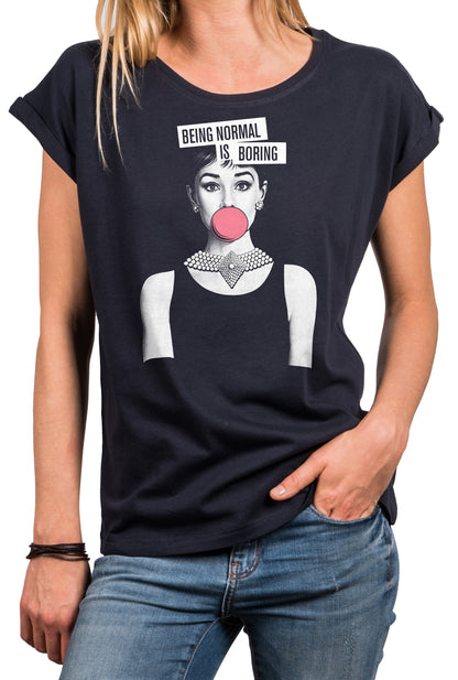May include: Dark navy blue t-shirt featuring a graphic of a woman with a pink bubblegum bubble and a pearl necklace. The text "BEING NORMAL IS BORING" is above the graphic. The shirt has rolled sleeves.