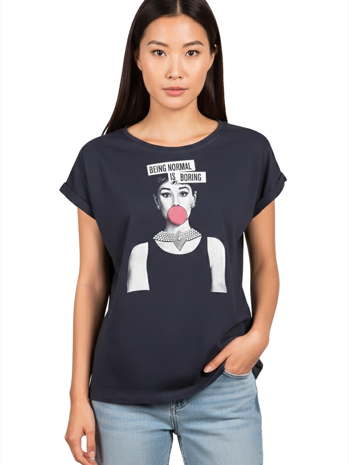 May include: Navy blue t-shirt featuring a graphic of a woman with a bubblegum bubble and the text "BEING NORMAL IS BORING". The shirt has rolled sleeves and a round neckline. The model is wearing blue jeans.