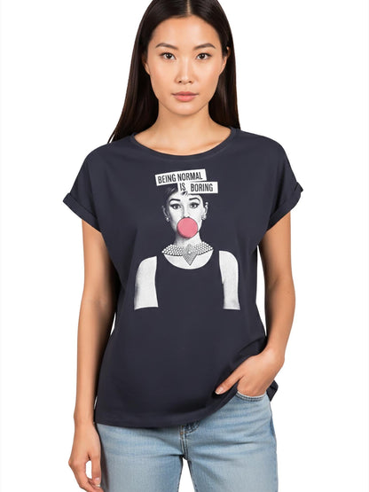 May include: Navy blue t-shirt featuring a graphic of a woman with a bubblegum bubble and the text "BEING NORMAL IS BORING". The shirt has rolled sleeves and a round neckline. The model is wearing blue jeans.