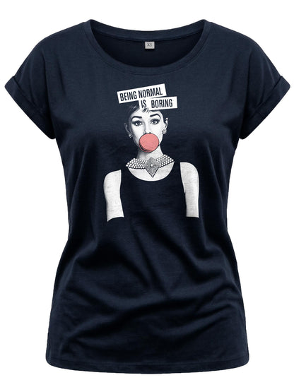 May include: Navy blue t-shirt featuring a graphic of a woman blowing a bubblegum bubble, with the text "BEING NORMAL IS BORING" above her head. The woman is wearing a necklace and earrings. The shirt has rolled-up sleeves.