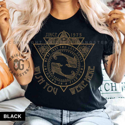May include: Black t-shirt with a gold graphic design featuring a triangle with an eye inside, two fish swimming in a circle, and the text "Since 1975 We're Just Two Lost Souls Swimming In A Fish Bowl Wish You Were Here".