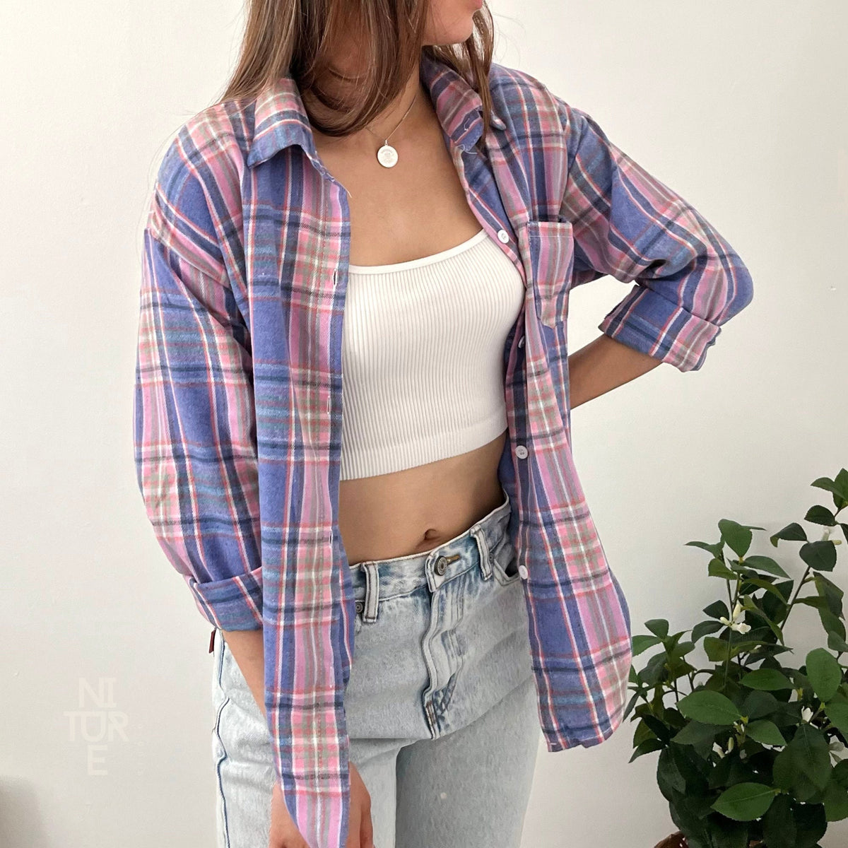 May include: A blue and pink plaid flannel shirt with a white tank top and light blue jeans.