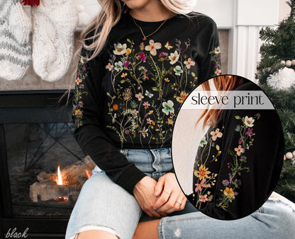 May include: Black long-sleeve shirt with a floral print. The print features a variety of flowers and leaves in shades of pink, yellow, and green. The shirt has a crew neck and long sleeves. The sleeve print is shown in a close-up.