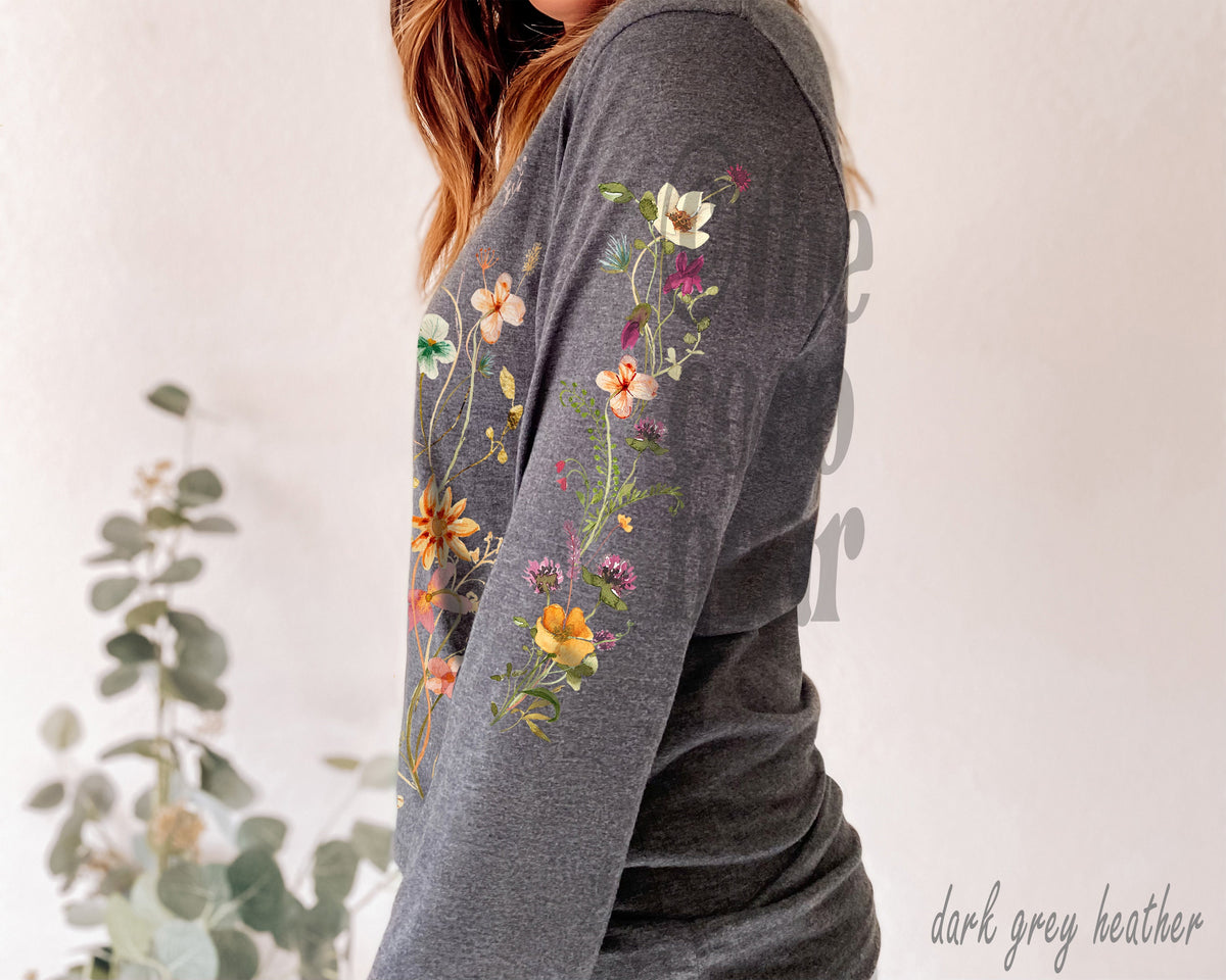 May include: A dark grey heather long-sleeve shirt with a floral design on the sleeve. The flowers are in shades of yellow, orange, pink, and purple.