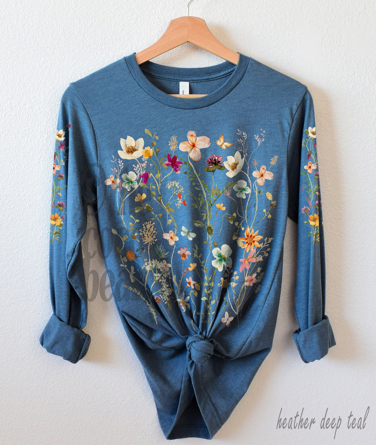 May include: A long-sleeved t-shirt in a heather deep teal color with a floral print featuring a variety of flowers in shades of pink, yellow, white, and green.