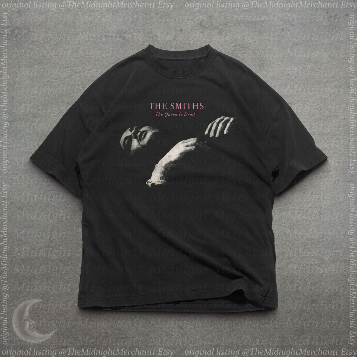 May include: A black short-sleeve t-shirt featuring a graphic print of a person lying down with their hand raised. The text THE SMITHS and The Queen Is Dead is printed in pink and white above the image. The shirt has a crew neckline and short sleeves.