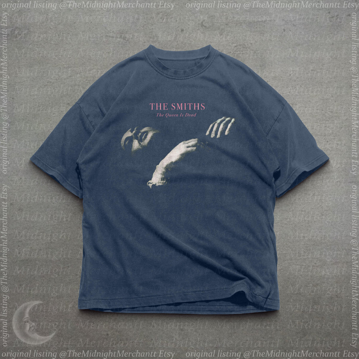 May include: A dark blue short-sleeve t-shirt featuring a graphic print of a person's face and hand. The text THE SMITHS and The Queen Is Dead is printed in pink and white above the graphic. The shirt has a crew neckline and a relaxed fit.