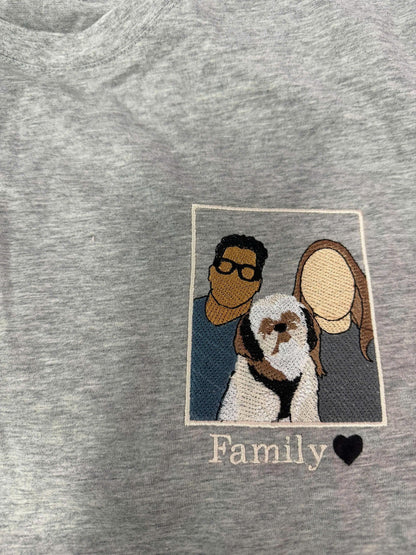 May include: A heather gray t-shirt featuring a rectangular embroidered patch. The patch depicts two faceless individuals and a small dog in the center. Below the patch, the word Family is embroidered in white script next to a black heart icon.