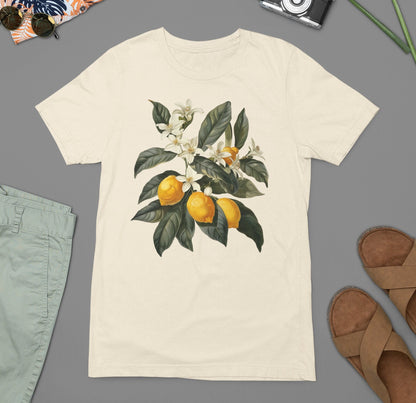 May include: A cream colored t-shirt with a graphic of a lemon tree branch with white blossoms and yellow lemons.