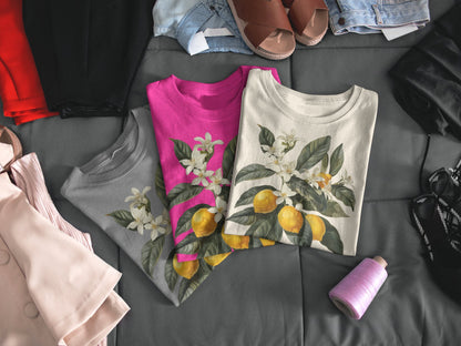 May include: Three t-shirts with a lemon tree design. The shirts are in gray, pink, and white.