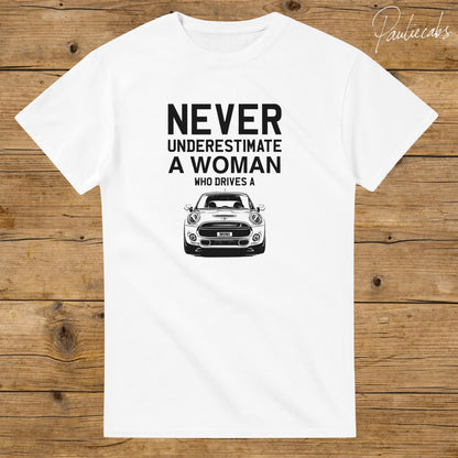 May include: A white short-sleeved t-shirt featuring black text that reads NEVER UNDERESTIMATE A WOMAN WHO DRIVES A above a black and white line art illustration of the front view of a Mini Cooper car with the word MINI on the license plate.