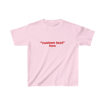 May include: A light pink t-shirt with short sleeves. The shirt features the red text "custom text" above the word "here" in red. The shirt is made of a soft material.