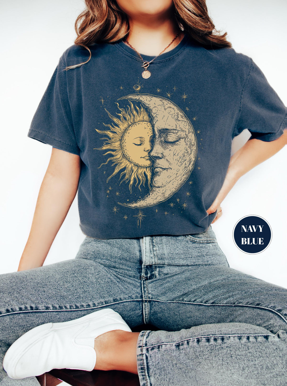 May include: Navy blue t-shirt featuring a celestial design of a sun and moon embracing. The sun is depicted with golden rays, while the moon has a detailed, textured appearance. The shirt has a relaxed fit and is paired with blue jeans.