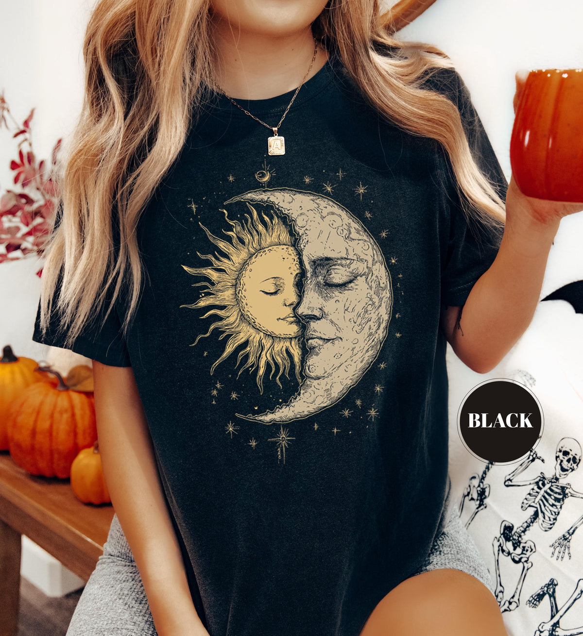 May include: Black t-shirt featuring a celestial design with a sun and moon embracing, surrounded by stars. The design is in a vintage style. The shirt has short sleeves and a round neckline. A black circle with the word "BLACK" is on the shirt.