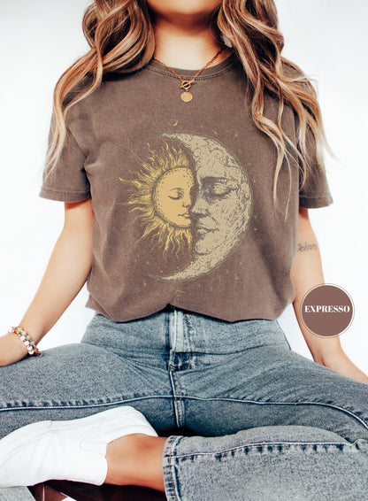 May include: Brown t-shirt featuring a celestial design with a sun and moon graphic. The sun is yellow, and the moon is beige. The shirt is worn with blue jeans. The word "EXPRESSO" is printed on a brown circle.