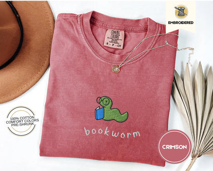 May include: A crimson red t-shirt with a green worm holding a book and the text "bookworm" embroidered on the front. The shirt is made of 100% cotton and is pre-shrunk.