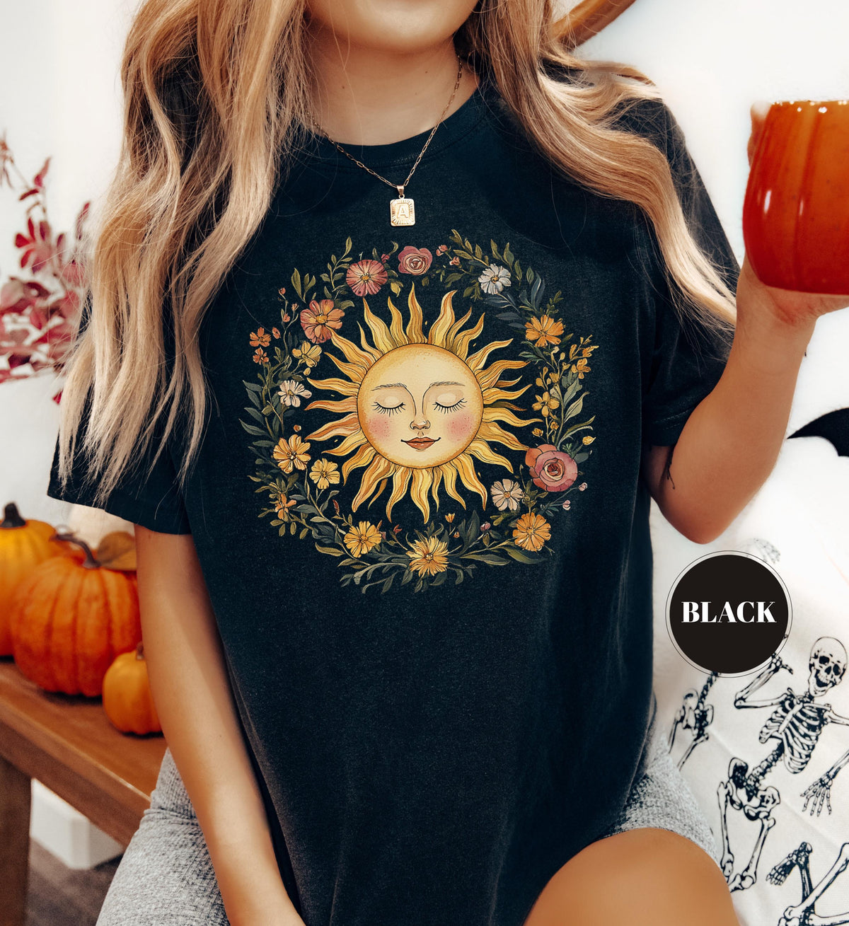 May include: Black t-shirt featuring a smiling sun graphic surrounded by a floral wreath. The sun has closed eyes and a serene expression. The shirt is a dark color, with a round "Black" sticker in the lower right corner.