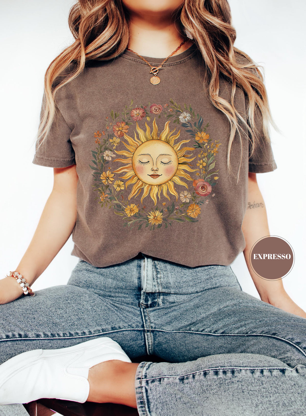 May include: Brown t-shirt featuring a sun graphic with a smiling face and floral wreath. The sun is yellow and orange, surrounded by colorful flowers and green leaves. The shirt has short sleeves and a crew neck.