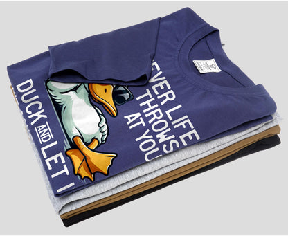 May include: A stack of folded t-shirts in navy blue, gray, brown, and black. The top shirt features a cartoon duck wearing sunglasses with the text "DUCK AND LET IT" and "WHATEVER LIFE THROWS AT YOU".