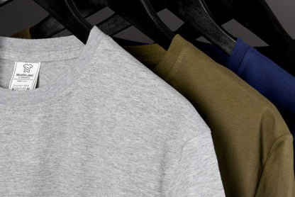 May include: Close-up of three t-shirts in gray, olive green, and navy blue hanging on a black hanger. The gray shirt has a tag that reads "Silver Lake T-Shirts" and "Designed in USA". The shirts are made of a soft material.