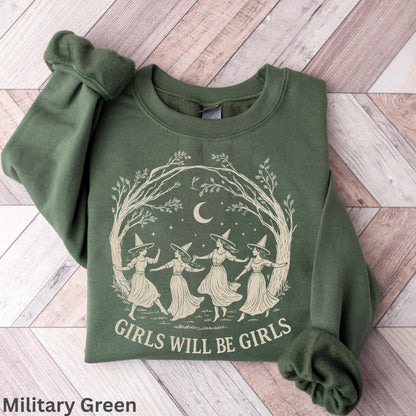 May include: A military green crewneck sweatshirt featuring a cream-colored graphic of four figures wearing pointed hats dancing in a circle under a crescent moon and tree branches, with the text "GIRLS WILL BE GIRLS" printed below the illustration.