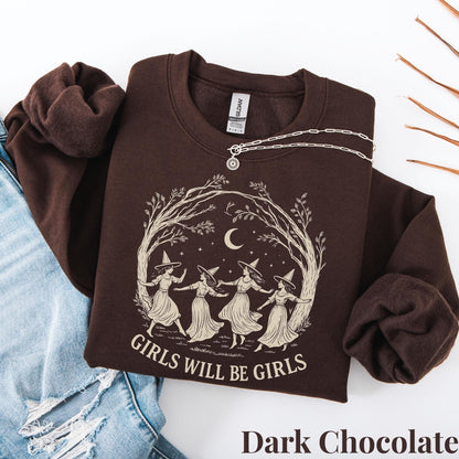 May include: A dark chocolate brown crewneck sweatshirt featuring a cream-colored graphic of four figures in pointed hats dancing in a circle under a crescent moon and tree branches, with the text "GIRLS WILL BE GIRLS" printed below the illustration.