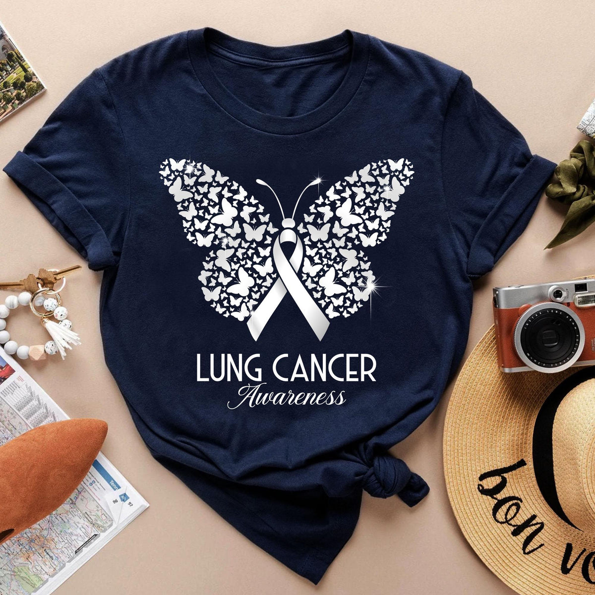 May include: Navy blue t-shirt featuring a white butterfly design composed of smaller butterflies, with a white ribbon in the center. The text "LUNG CANCER Awareness" is printed below the butterfly. The shirt is a classic crew neck.