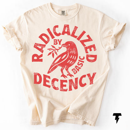 May include: Cream-colored t-shirt with rolled-up sleeves. The front features a distressed red graphic of a bird holding a sprig, encircled by the words "RADICALIZED BY BASIC DECENCY."