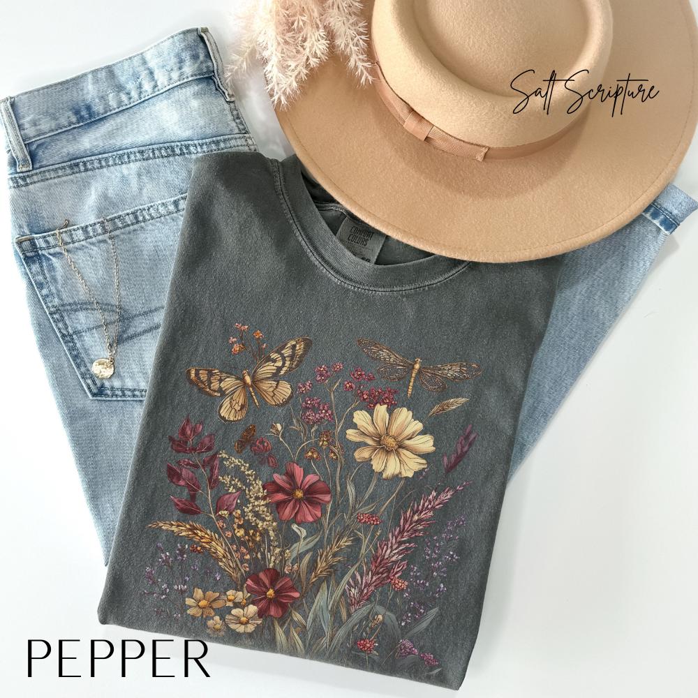 May include: A gray t-shirt with a floral and insect design, including butterflies and a dragonfly, is displayed on top of blue jeans. A tan hat with a brown band and the text "Salt Scripture" is also visible. The word "PEPPER" is at the bottom.