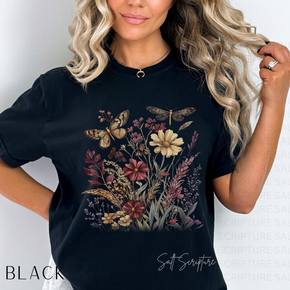 May include: Black t-shirt featuring a floral and insect design. The graphic includes butterflies, a dragonfly, and various flowers in shades of brown, red, and yellow. The word "BLACK" is printed on the bottom left.