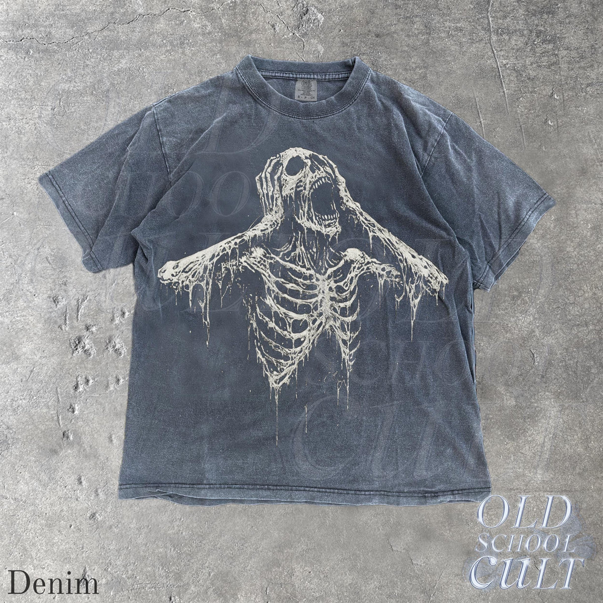 May include: Denim-colored t-shirt with a distressed graphic of a screaming skeleton. The shirt has short sleeves and a crew neck. The text "OLD SCHOOL CULT" is printed on the bottom right corner. The word "Denim" is printed on the bottom left corner.