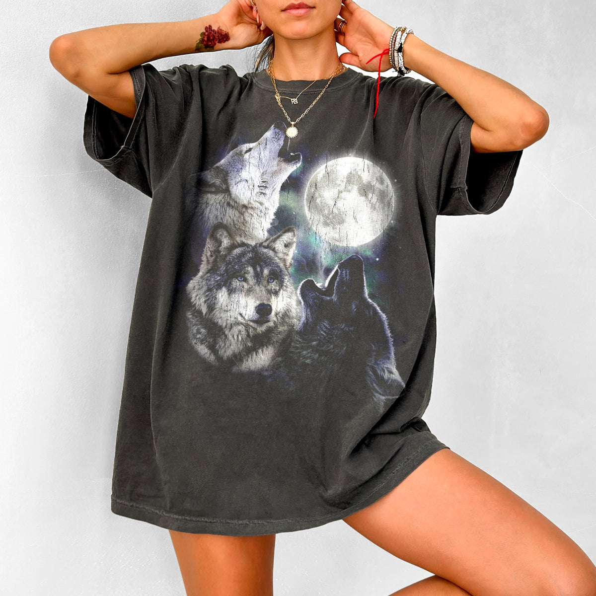 May include: Dark gray t-shirt featuring a graphic of three wolves howling at a full moon. The design includes a detailed illustration of the wolves and the moon against a starry background. The shirt has short sleeves and a relaxed fit.