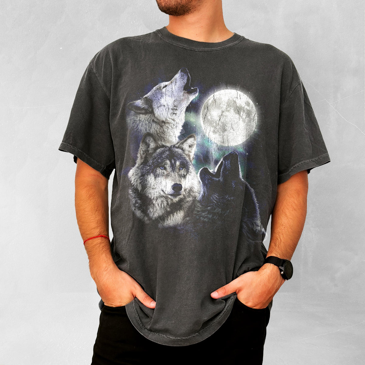 May include: Dark gray t-shirt featuring a graphic of three wolves howling at a full moon. The wolves are depicted in shades of gray and black, with the moon in the background. The shirt has a vintage, worn look.