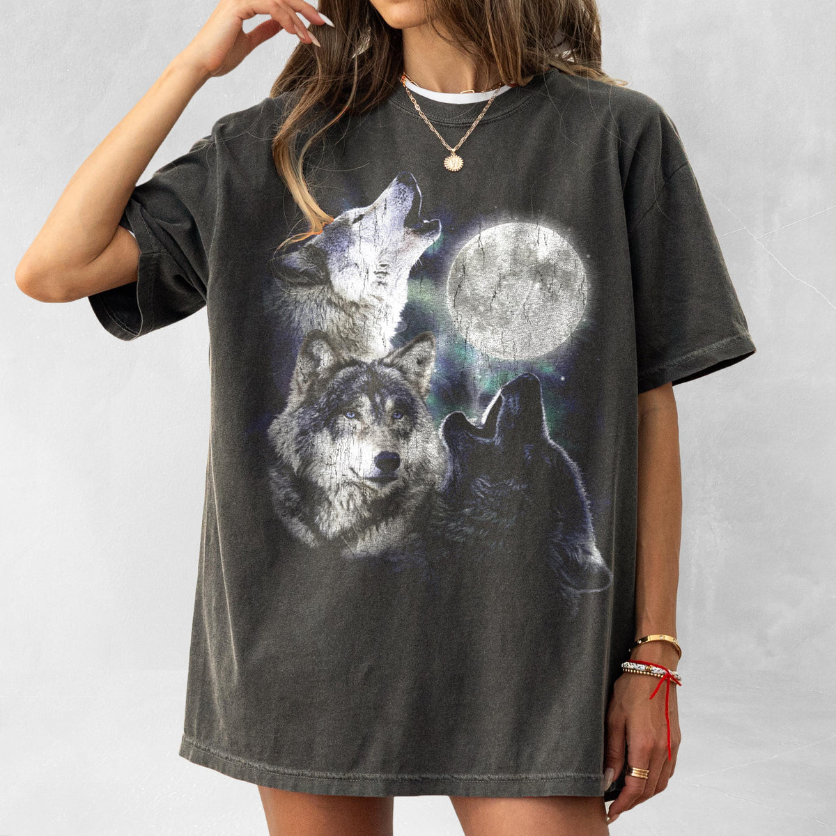May include: Dark gray t-shirt featuring a graphic of three wolves howling at a full moon. The design includes detailed illustrations of the wolves and a bright, glowing moon against a starry background. The shirt has a vintage, worn look.