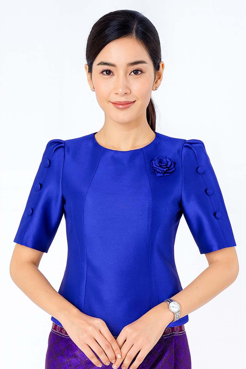 May include: A vibrant royal blue short-sleeved blouse featuring a round neckline, structured puff sleeves with three decorative buttons on each side, and a matching fabric rose pinned to the upper left chest area, crafted from a smooth satin-like fabric.
